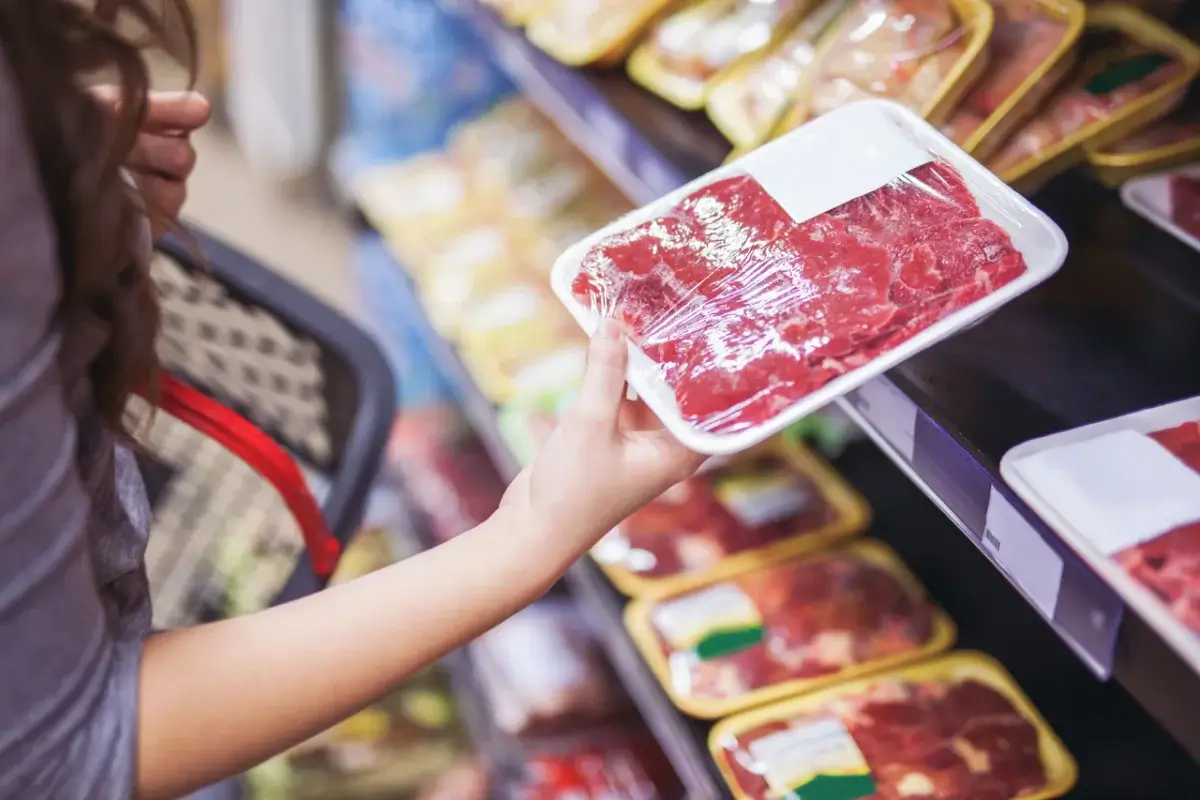 A person holds a meat package in a store.